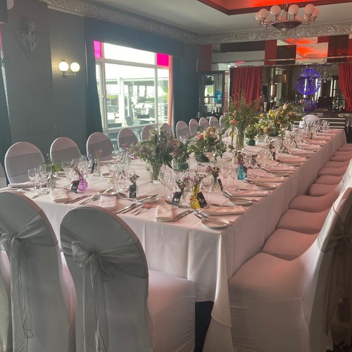 Elegant private dining room with long banquet table, white chair covers tied with grey bows, mixed floral centerpieces and crystal glassware.