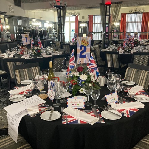 Elegant hotel banquet set for a British-themed dinner: round tables with black linen, Union Jack napkins and flags, floral centerpiece.