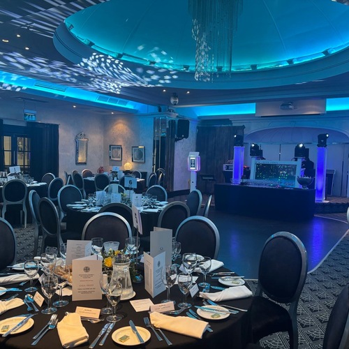 Hotel ballroom for gala: round tables with black linens, glassware and menus; illuminated dome, blue uplighting.