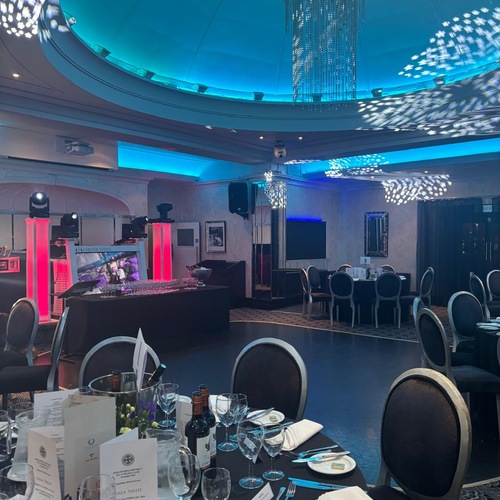 Elegant hotel ballroom set for dinner: round tables with wine and place settings, dance floor, DJ booth with red lights, blue domed ceiling