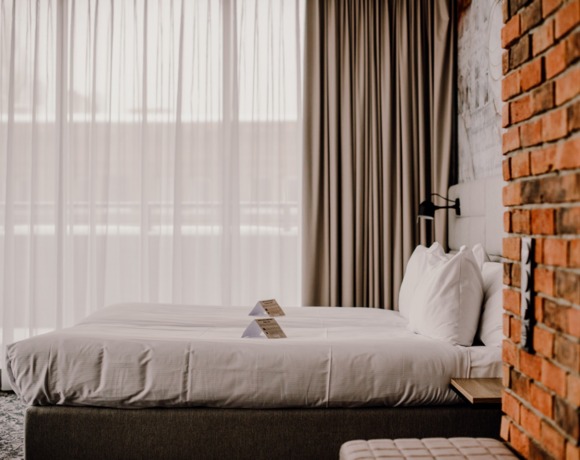 Nowoczesny pokój hotelowy z dwoma łóżkami, białą pościelą, lampką przy łóżku, ceglaną ścianą i miękkimi zasłonami