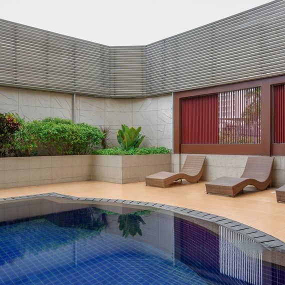 Private hotel pool courtyard with blue-tiled plunge pool, three woven sun loungers on tiled deck and planted privacy walls.