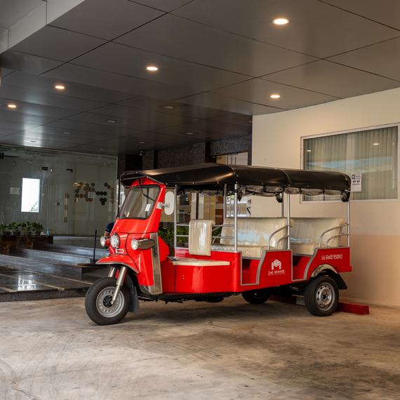 Red hotel shuttle tuk-tuk parked under a covered porte-cochere with recessed ceiling lights, steps and glass lobby doors