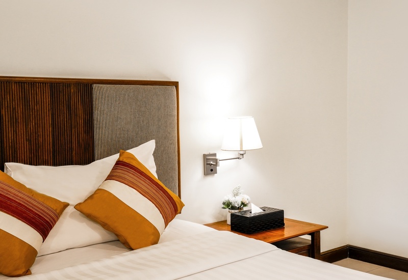 Queen bed with slatted wood headboard and padded panel, white linens, mustard-striped pillows, bedside lamp and flowers