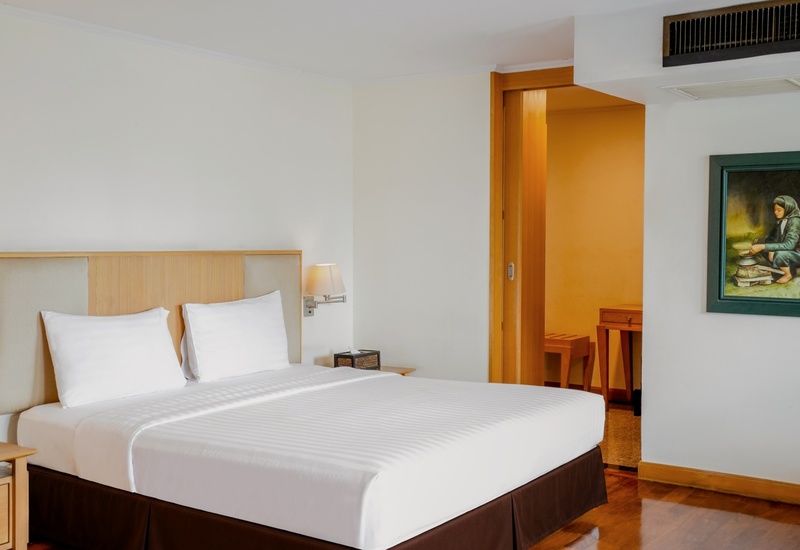 Bright guest room with king bed in white linens, wooden headboard, wall lamps, bedside table, framed painting, sliding door.