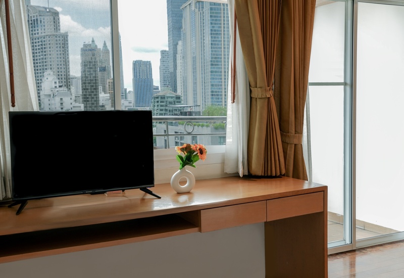 Hotel desk with flat-screen TV, vase of orange flowers, floor-to-ceiling windows and balcony overlooking city skyline