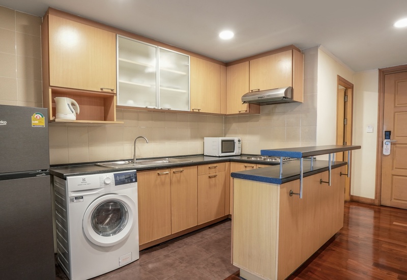 Self-catering kitchenette with wooden cabinets, fridge, washing machine, microwave, stovetop, sink and breakfast bar.