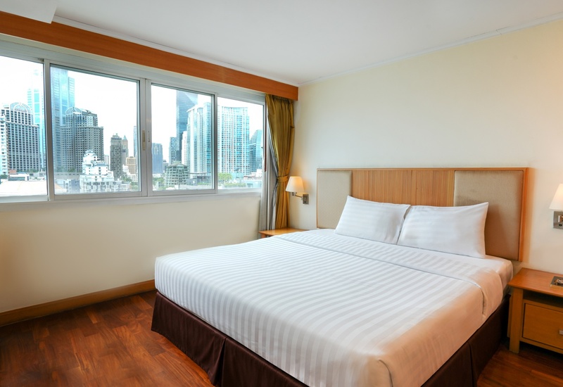 City-view hotel room with king bed, crisp white linens, wood floors, bedside lamps and large windows