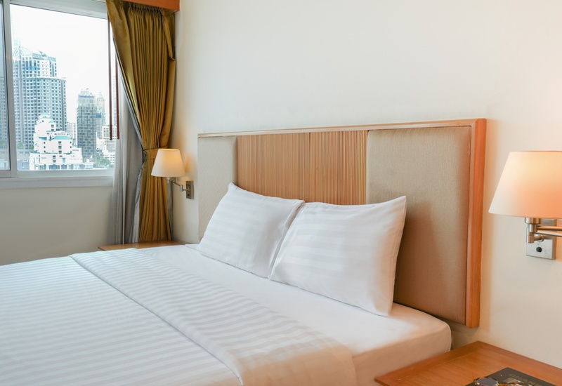 Bright hotel room with king bed, crisp white linens, padded wood headboard, bedside lamps and city skyline visible through window.