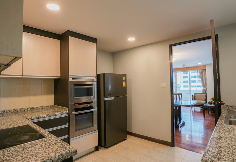 Kitchenette with granite counters, electric cooktop, built-in oven and fridge, doorway to sunlit living area and balcony view.