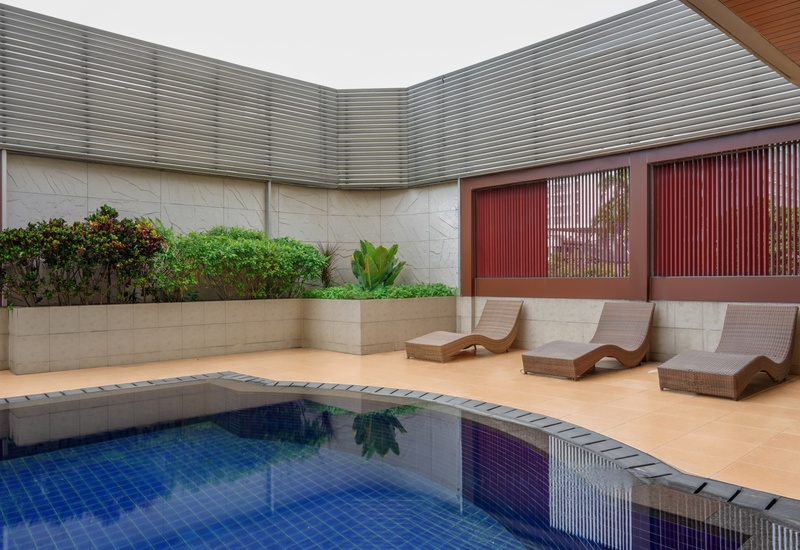 Private hotel pool courtyard with blue-tiled plunge pool, three woven sun loungers on tiled deck and planted privacy walls.