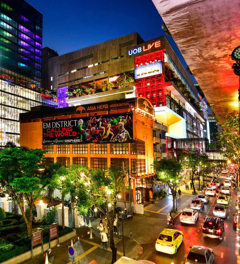 Vibrant night retail district with illuminated glass mall, rooftop terraces, colorful LED façade, taxis and skywalk