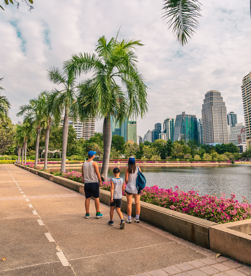 Palm-lined lakeside promenade with pink flowerbeds and city skyline; family walking along the waterfront path.