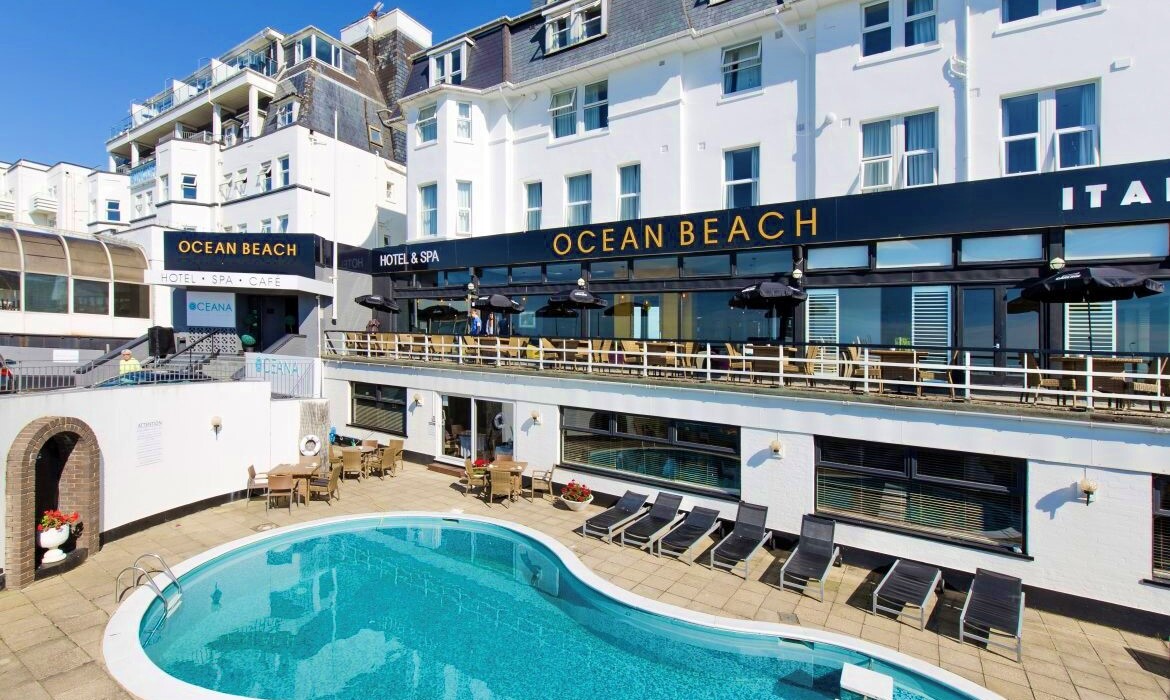 Ocean Beach Hotel & Spa with curved outdoor pool, sun loungers and terrace café seating under black umbrellas