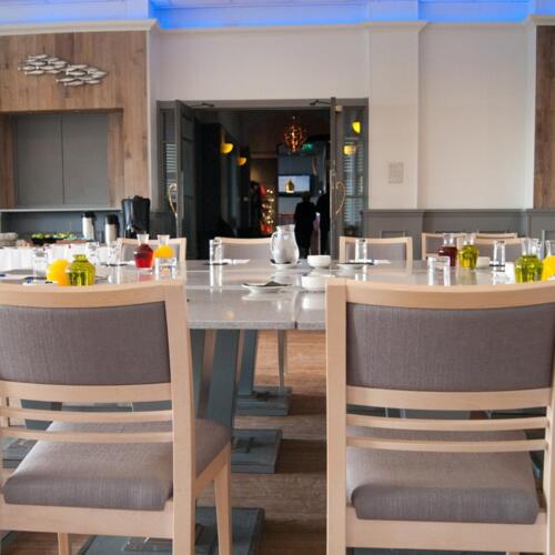 Bright hotel meeting room with long table set for breakfast/meeting, wood-paneled walls, blue cove lighting, juice decanters