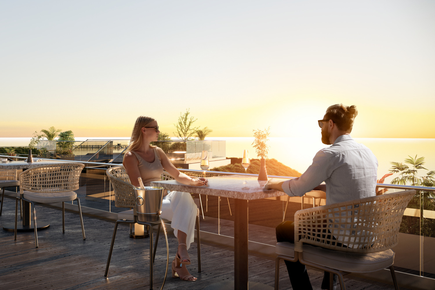 Para relaksuje się przy zachodzie słońca na tarasie dachowym hotelu nad morzem, marmurowy stolik, wiklinowe fotele i kieliszki