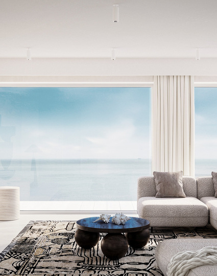 Przestronny salon przy plaży z oknami od podłogi do sufitu, miękką sofą modułową, wzorzystym dywanem, rzeźbiarską dekoracją i rozległym widokiem na morze.