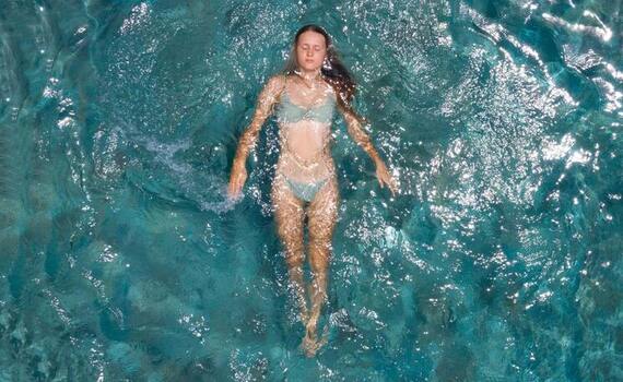 Gość unoszący się na plecach w krystalicznie turkusowym basenie hotelowym, słoneczne refleksy na wodzie, relaksacyjna atmosfera