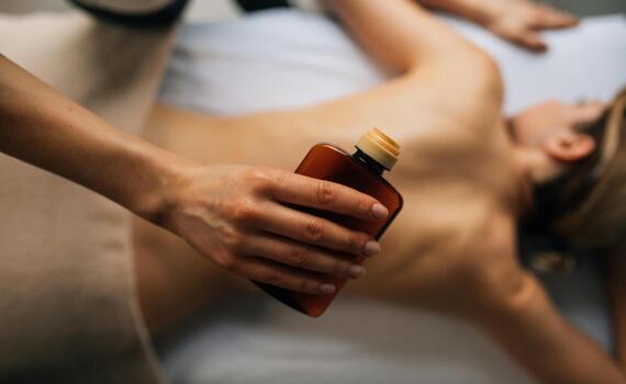 Therapeut gießt warmes Massageöl aus bernsteinfarbener Flasche auf den nackten Rücken eines Gastes bei entspannender Spa-Behandlung