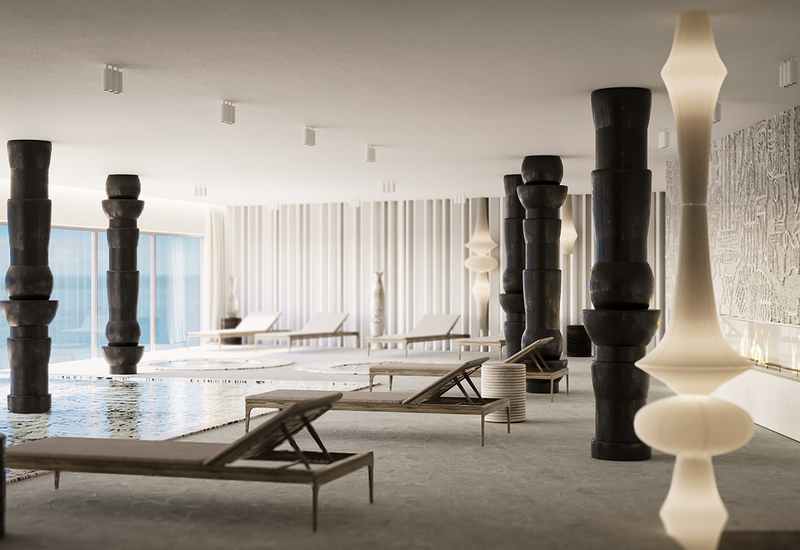 Strefa spa wewnątrz z płytkim basenem, leżakami, rzeźbiarskimi czarnymi filarami, panoramicznymi oknami z widokiem na morze i kominkiem