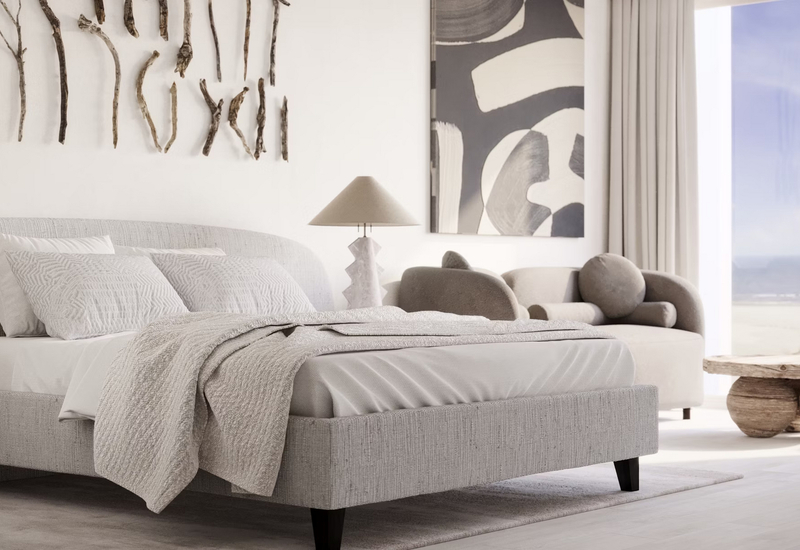 Nadmorska suita z dużym łóżkiem w teksturowanej pościeli, zaokrągloną sofą, rzeźbiarską lampą, dekoracją z drewna i widokiem na morze.