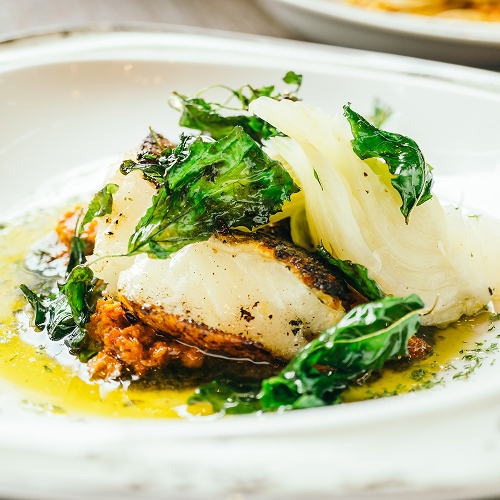 Smażona biała ryba z duszonym koprem włoskim, chrupiącymi zielonymi liśćmi, pomidorowym ragù i masłowo-cytrynowym sosem