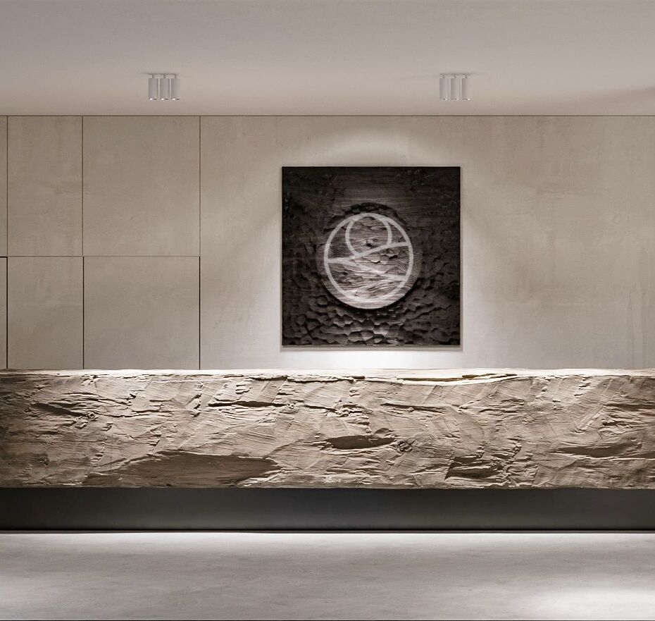 Minimalistyczna recepcja z rzeźbionym kamiennym blatem, rzeźbiarską lampą, fakturowym obrazem i ciepłym oświetleniem.