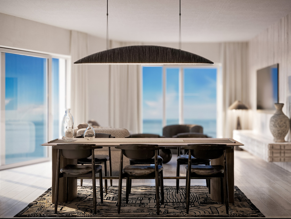 Jadalnia z widokiem na ocean w salonie typu open-space, drewniany stół na sześć osób pod dużą lampą, okna od podłogi do sufitu i stonowane nadmorskie wnętrze.