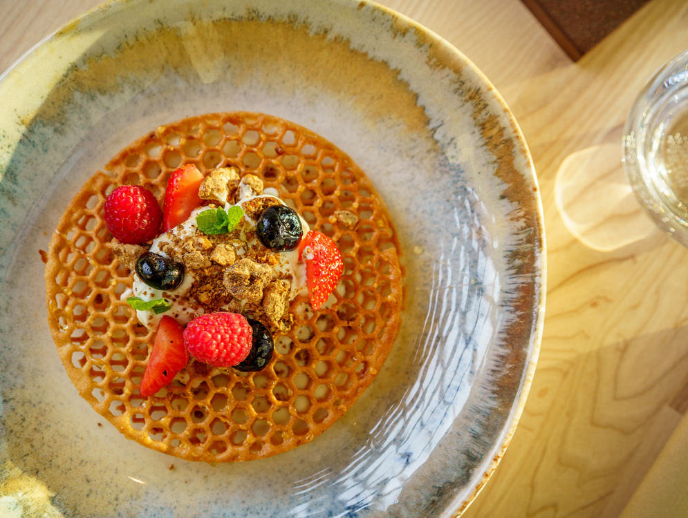 Chrupiący waflowy krążek z kremem, malinami, truskawkami, borówkami, granolą i miętą na ceramicznym talerzu