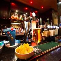 Cozy pub bar with illuminated beer taps (Guinness), a pint, Pepsi dispenser, bowl of crisps and backlit spirits.