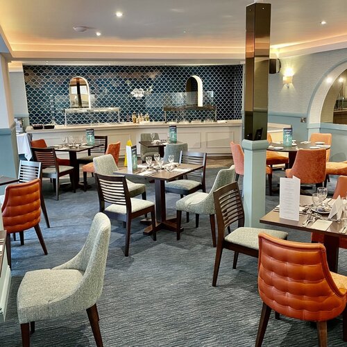 Bright hotel dining room with blue fish-scale tile buffet wall, set tables, mixed upholstered chairs and warm lighting