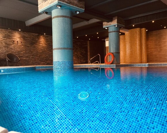 Indoor hotel pool with blue mosaic tiles, round tiled columns, warm stone walls, recessed lighting and lifebuoy.