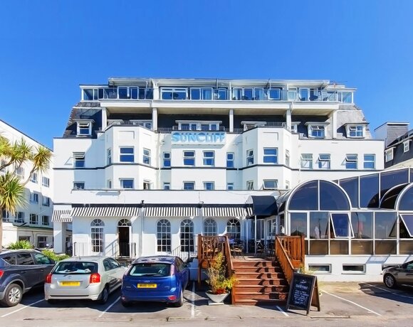White Suncliff hotel with rooftop terraces and glass balconies, arched glass conservatory, wood steps, palm trees, cars