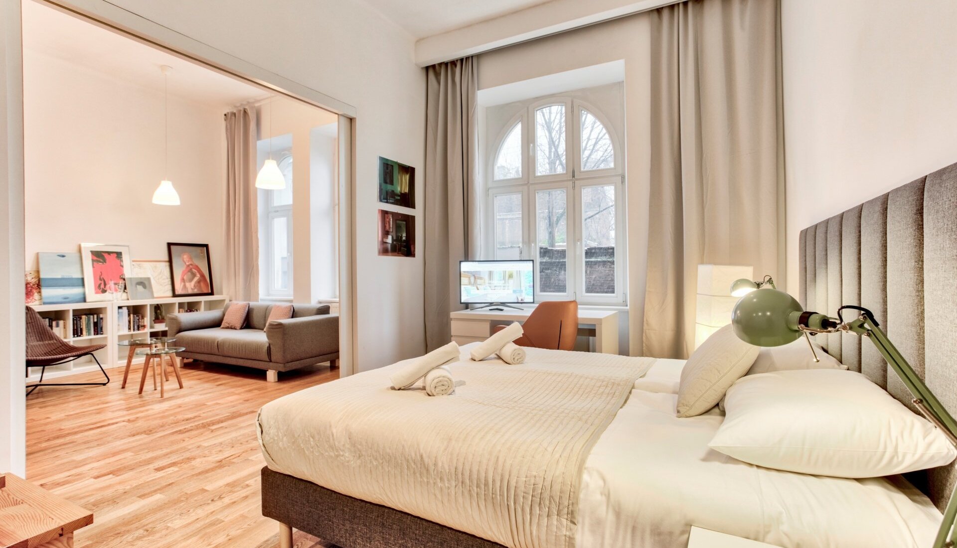 Jasny pokój hotelowy z dużym łóżkiem, biurkiem przy oknie, sofą i nowoczesnym wyposażeniem w eleganckim stylu.