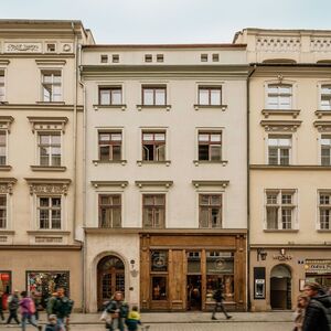 Historyczna kamienica w centrum z drewnianym wejściem butikowego hotelu, parterowe kawiarnie i przechodnie.