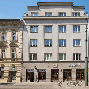Fasada miejskiego hotelu w beżowym modernistycznym budynku, kawiarnia na parterze, stojak na rowery, przechodnie.