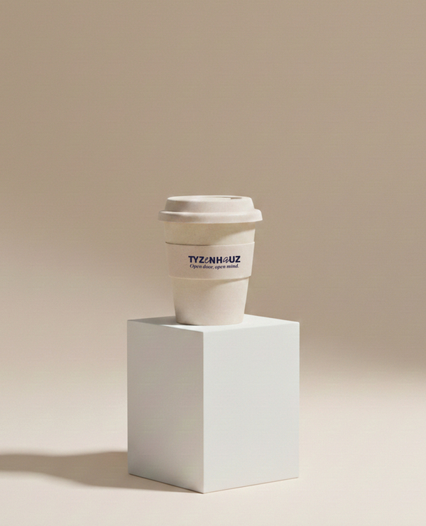 Kubek kawy na wynos z logo 'TYZENHAUZ' na białym postumencie, minimalistyczna ciepła beżowa estetyka