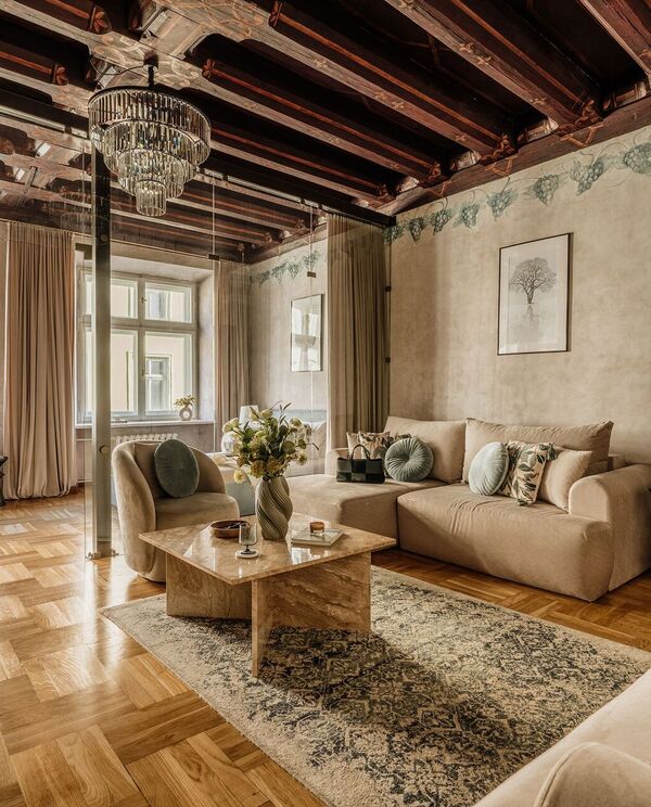 Elegant apartment lounge with wooden beams, crystal chandelier, glass partition, beige sofas and marble table.