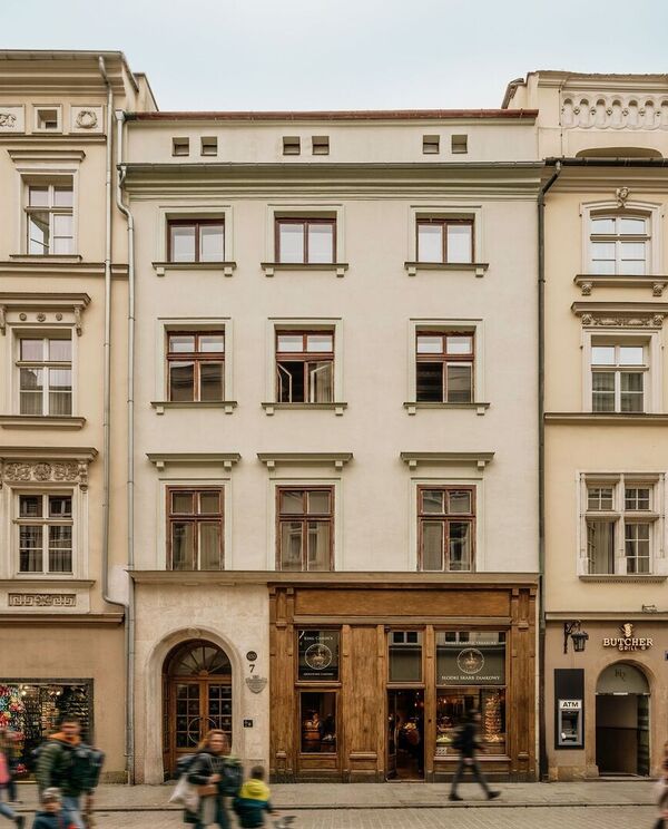 Historyczna kamienica w centrum z drewnianym wejściem butikowego hotelu, parterowe kawiarnie i przechodnie.