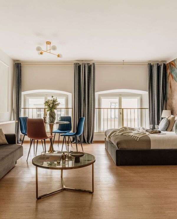 Spacious modern studio suite with king bed, sofa, dining table, floral accent wall, arched windows and soft lighting.