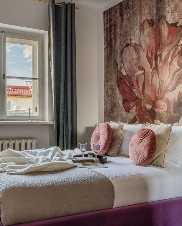 Boutique double room with plush bed, floral wall mural, velvet purple bed base, round pink cushions and rooftop view