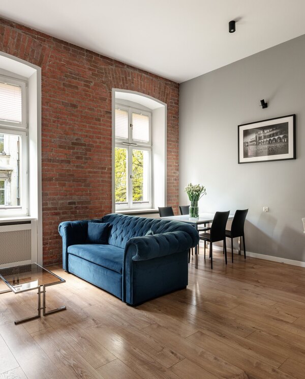 Loft-style suite with exposed brick and arched windows, blue velvet sofa, dining table and a modern kitchenette