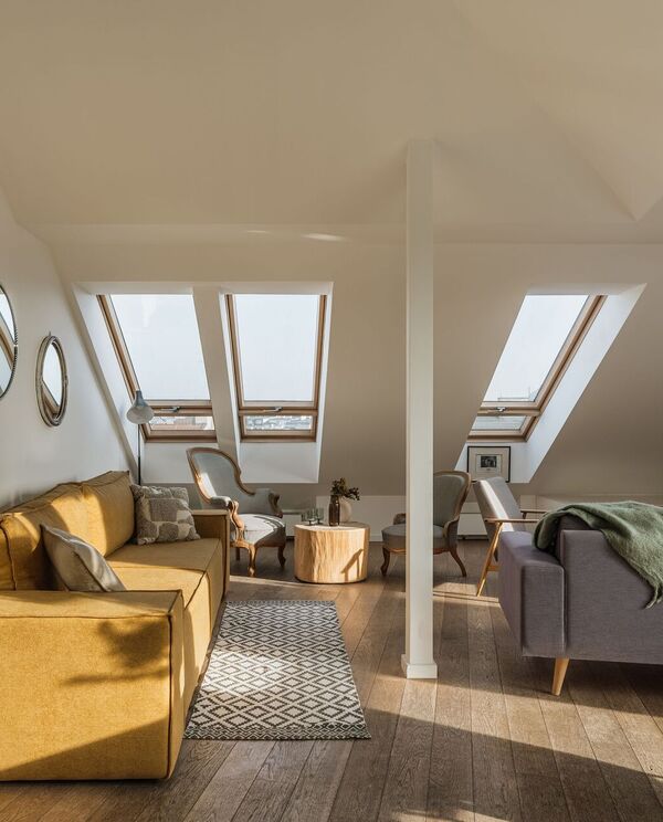 Attic-suite lounge with sloped ceiling, four skylights, mustard sofa, armchairs, wooden stump table and warm natural light over hardwood floors