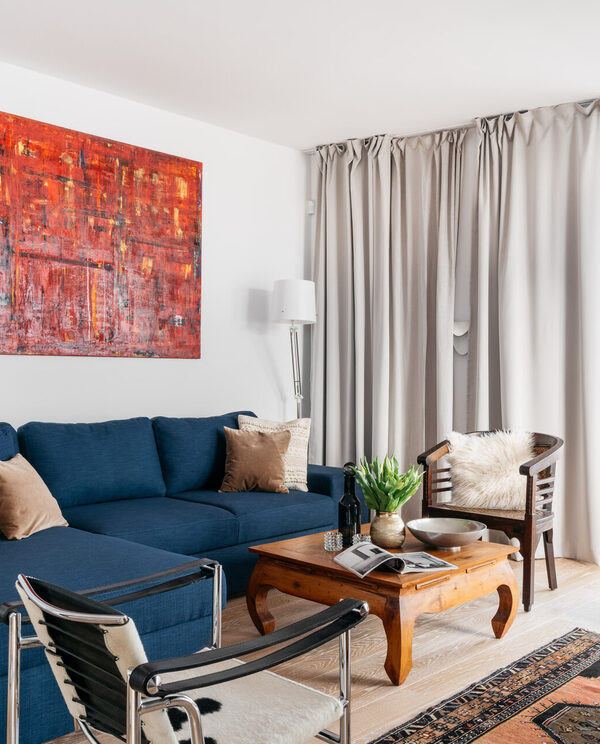 Bright boutique suite lounge with deep-blue sofa, wooden coffee table, bold red abstract painting, floor lamps and city-view balcony.