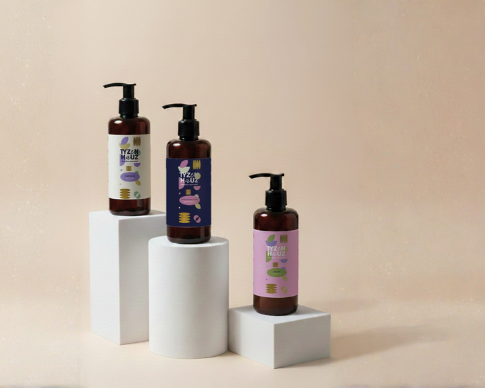 Trzy bursztynowe butelki z pompkami na białych podstawach — luksusowy szampon, żel i mydło dla gości