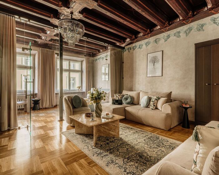 Elegant apartment lounge with wooden beams, crystal chandelier, glass partition, beige sofas and marble table.