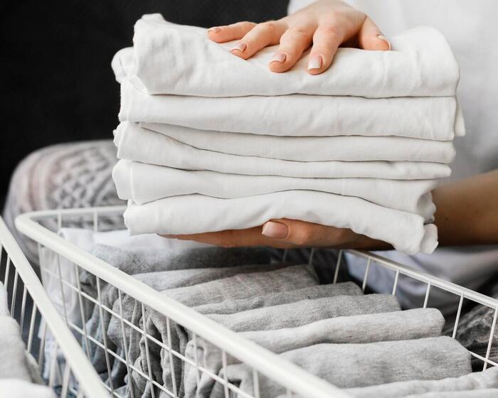 Ręce personelu trzymają starannie złożone białe pościele nad koszami z czystymi ręcznikami i prześcieradłami