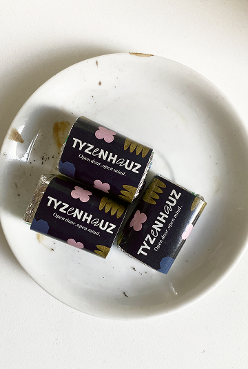 Trzy małe czekoladki owijane w czarne papierki z różowymi kwiatami, podane na białym talerzu.