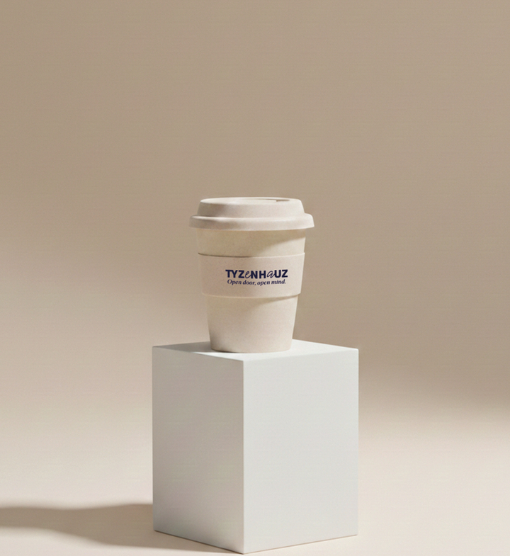 Kubek kawy na wynos z logo 'TYZENHAUZ' na białym postumencie, minimalistyczna ciepła beżowa estetyka