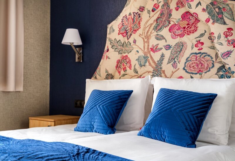 Bed with white bedding, navy pillows and colorful floral headboard in a stylish hotel room.
